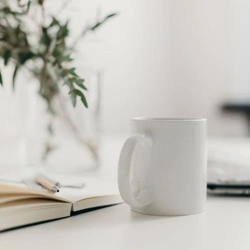 Bijela šalica za kavu na stolu pokraj knjige